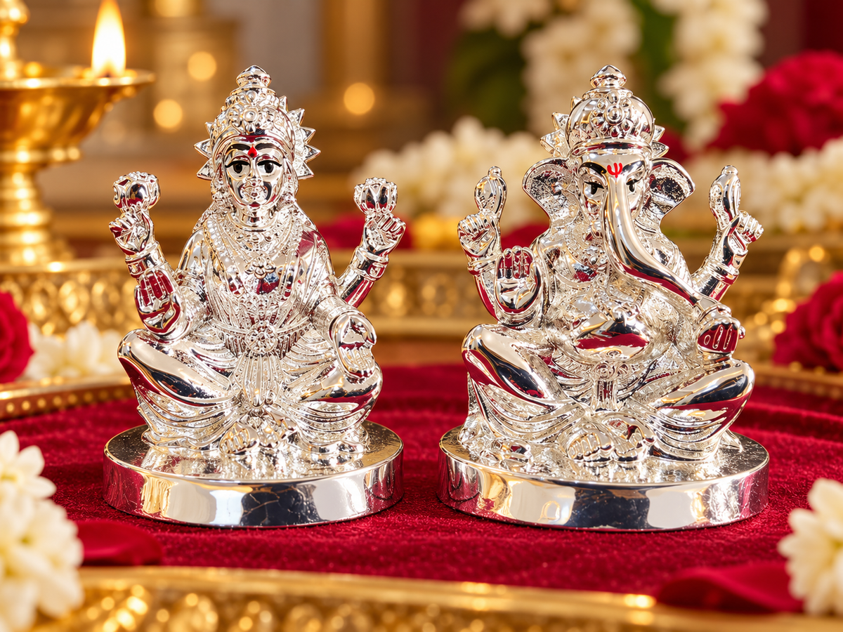 Silver-toned Lakshmi and Ganesha idols with detailed crowns and facial accents in a festive setting.